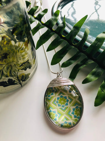 A large silver oval pendant with a mixture of green tones in a retro effect print and silver wire detailing