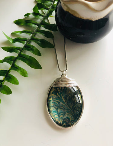A large silver oval pendant with a green and gold marble effect print