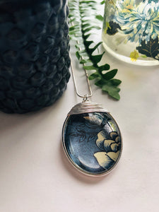 A large silver oval pendant with a blue and white vintage print