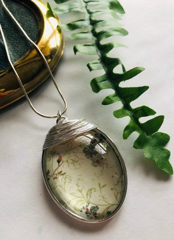 A large silver oval pendant with a light green botanical print pendant